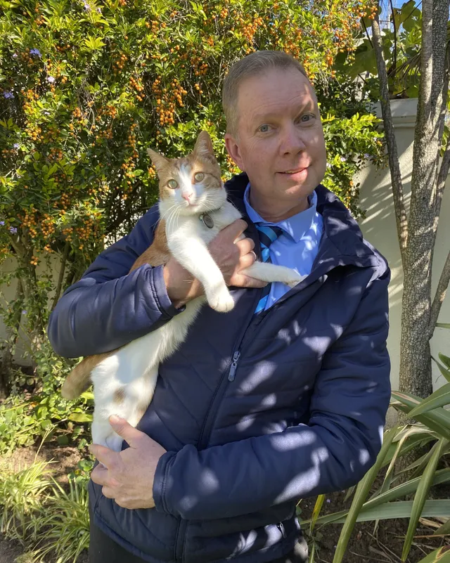 Leigh De Wet holding a white and grey cat in a garden